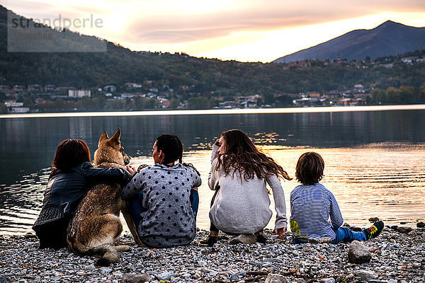 Rückansicht eines Jungen mit Familie und Hund am Fluss in der Abenddämmerung  Vercurago  Lombardei  Italien