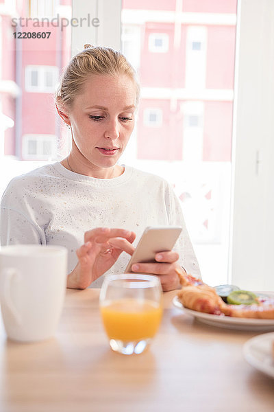 Junge Frau mit Smartphone-Touchscreen am Frühstückstisch