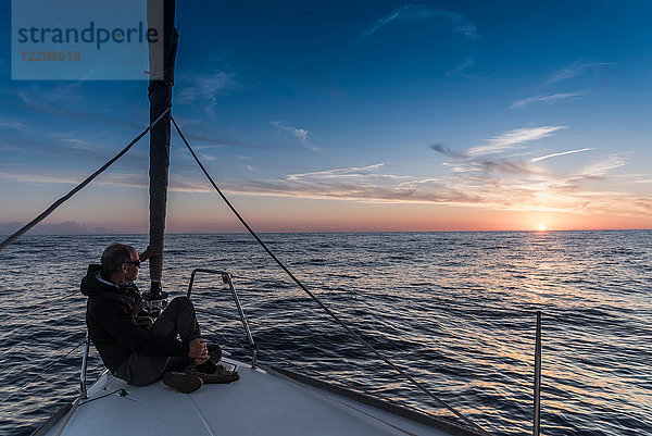 Älterer Mann sitzt an Bord einer Yacht und betrachtet Sonnenuntergang  Porquerolles  Provence-Alpes-Cote d'Azur