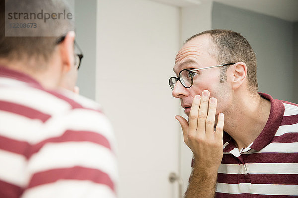 Über-Schulter-Ansicht eines reifen Mannes  der sein Gesicht im Badezimmerspiegel betrachtet