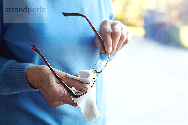 Ältere Frau reinigt Brille mit Tuch  mittlerer Abschnitt