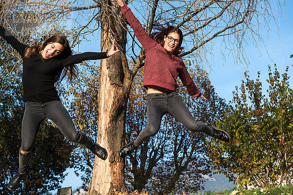 Zwei junge Frauen springen mitten in der Luft in einem Waldgebiet  Calolziocorte  Lombardei  Italien
