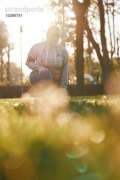 Kurvenreiche junge Frau  die im Park trainiert  sich nach vorne beugt und hockt