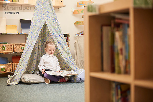 Schulmädchen sitzt auf dem Boden und liest im Klassenzimmer der Grundschule