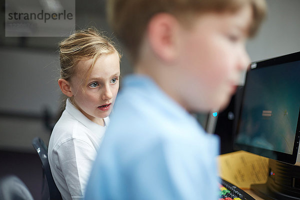 Schulmädchen und Junge benutzen Computer im Klassenzimmer der Grundschule