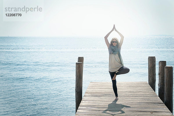 Frau auf dem Pier beim Balancieren auf einem Bein in Yoga-Pose