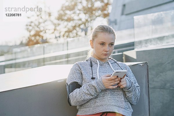 Kurvenreiche junge Frau in Ausbildung  mit Smartphone an Wand gelehnt