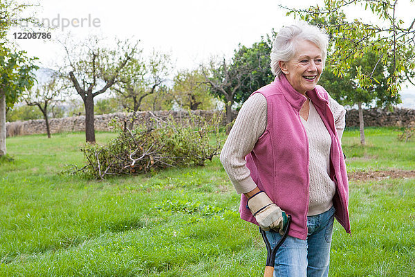 Ältere Frau im Garten  lehnt sich an Gartengerät an