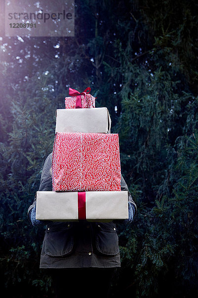 Frau trägt einen Stapel Weihnachtsgeschenke  Tanne im Hintergrund