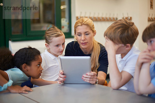 Lehrer mit Schülerinnen und Schülern  die sich im Klassenzimmer der Grundschule ein digitales Tablet ansehen