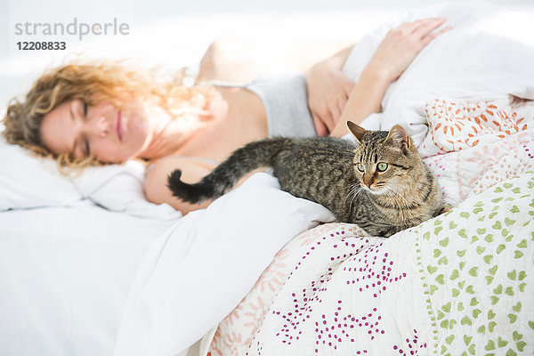 Frau zu Hause  schläft im Bett  Hauskatze liegt neben ihr