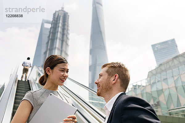 Junger Geschäftsmann und junge Geschäftsfrau bewegen sich auf der Rolltreppe im Finanzzentrum Shanghai  Shanghai  China