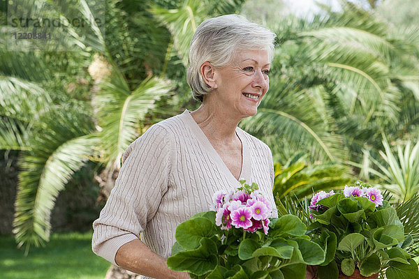 Ältere Frau im Garten  Pflanzen haltend