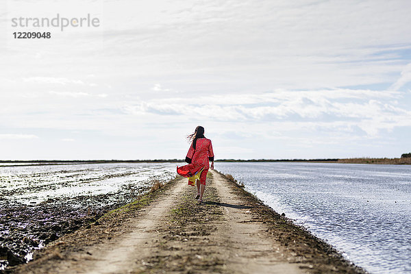 Rückansicht einer jungen Asiatin auf einem Feldweg auf dem Meer in traditioneller Kleidung  Tarragona  Katalonien  Spanien