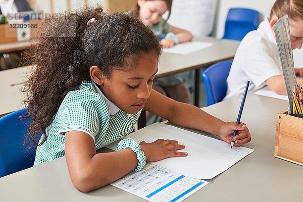 Schulmädchen schreibt in der Grundschulstunde am Klassenpult