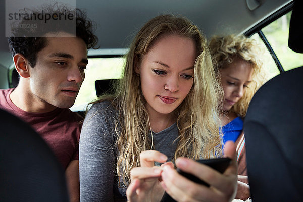 Freunde auf dem Rücksitz eines Autos schauen auf ein Smartphone