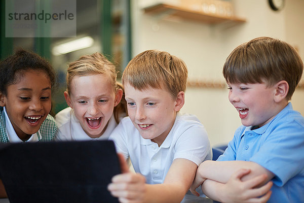 Schülerinnen und Schüler lachen über das digitale Tablet im Klassenzimmer der Grundschule