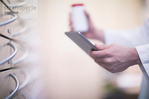 Männlicher Apotheker hält Pillenflasche und digitale Tablette in der Apotheke  Nahaufnahme der Hand