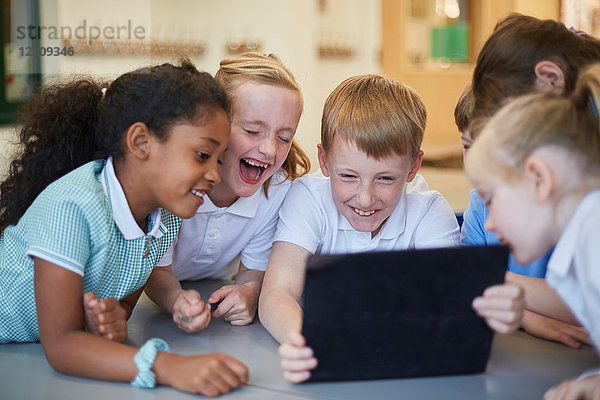 Schülerinnen und Schüler lachen über das digitale Tablet im Klassenzimmer der Grundschule