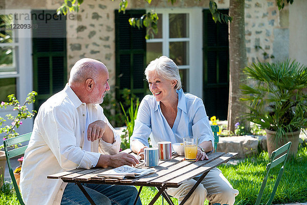 Älteres Ehepaar sitzt im Garten  Kaffeetassen auf dem Tisch