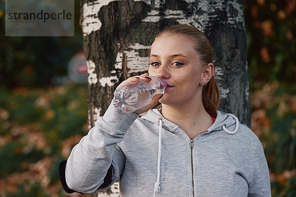 Porträt einer jungen Frau  die im Park trainiert und Flaschenwasser trinkt