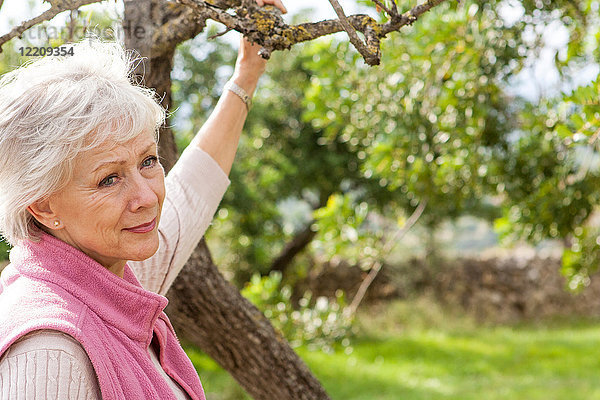 Porträt einer älteren Frau im Garten  die einen Baumzweig hält