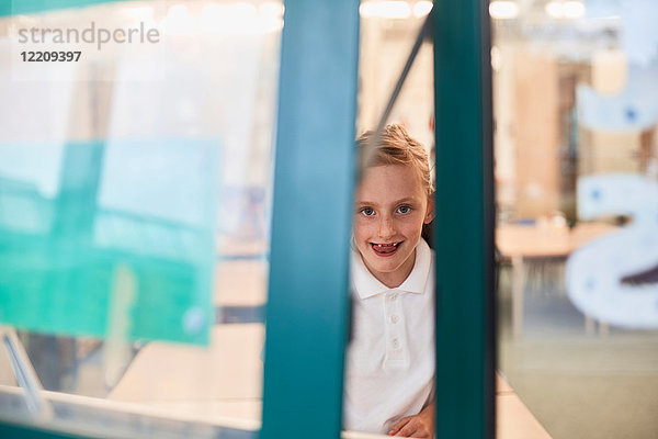 Porträt einer Schülerin  die in der Grundschule durch ein Klassenzimmerfenster schaut