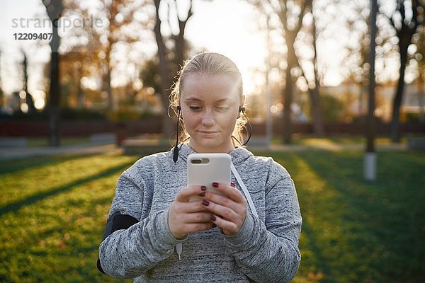 Junge Frau  die im Park trainiert und sich ein Smartphone anschaut