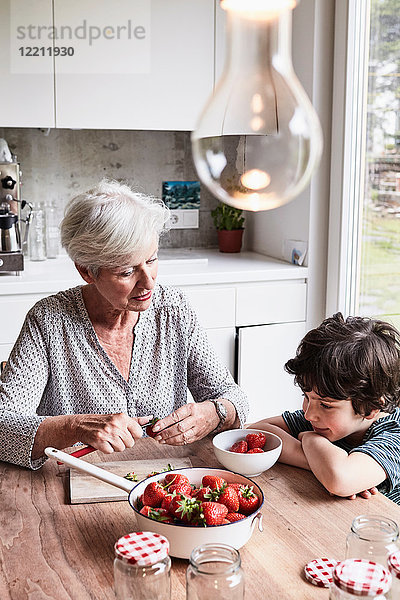 Großmutter sitzt am Küchentisch  bereitet Erdbeeren zu  Enkel sitzt neben ihr und schaut zu