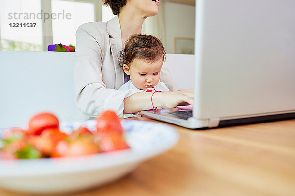 Mutter benutzt Laptop mit auf dem Schoß sitzendem Mädchen