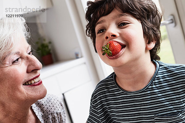 Enkel isst Erdbeere  Großmutter sitzt neben ihm und lächelt