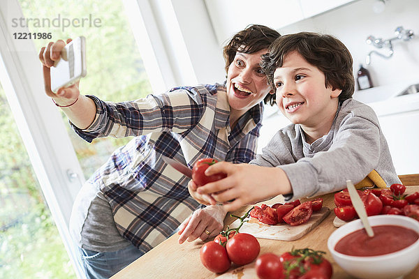 Mutter und Sohn bereiten das Essen in der Küche zu  Mutter nimmt sich selbst mit dem Smartphone