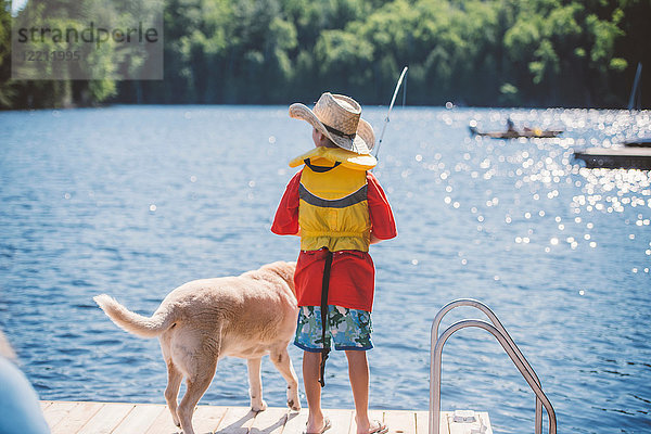 Rückansicht von Hund und Junge mit Cowboyhut beim Angeln vom Seepier