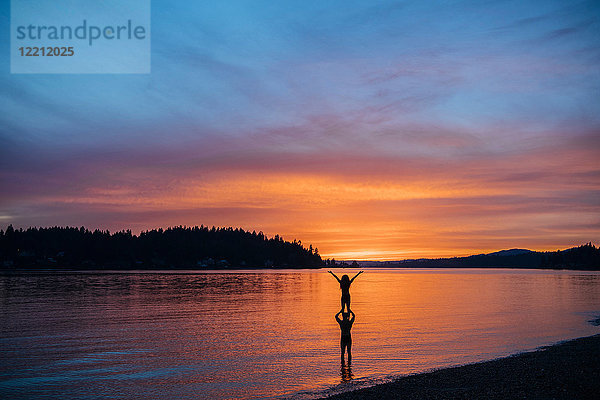 Ehepaar praktiziert Yoga am Strand bei Sonnenuntergang