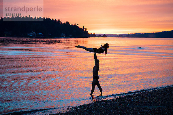 Ehepaar praktiziert Yoga am Strand bei Sonnenuntergang