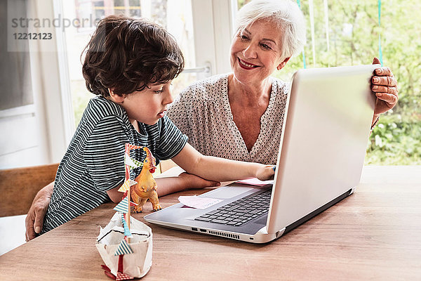 Großmutter und Enkel am Tisch sitzend  mit Laptop
