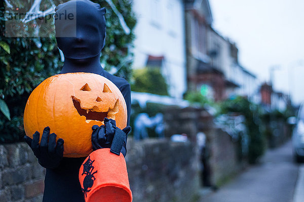 Porträt eines Jungen in Halloween-Kostüm  der einen Kürbis und einen Eimer mit Süßem oder Sauberem hält