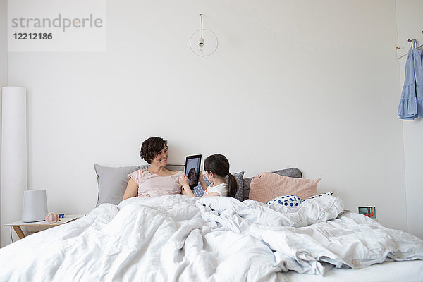 Mutter und Tochter entspannen sich im Bett  Tochter fotografiert Mutter mit digitalem Tablett