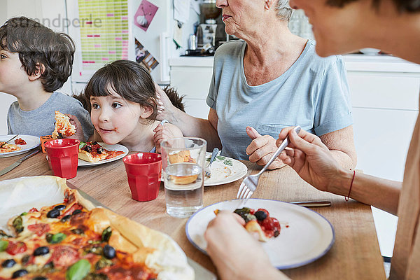 Drei-Generationen-Familie sitzt am Küchentisch und isst Pizza