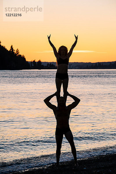 Ehepaar praktiziert Yoga am Strand bei Sonnenuntergang