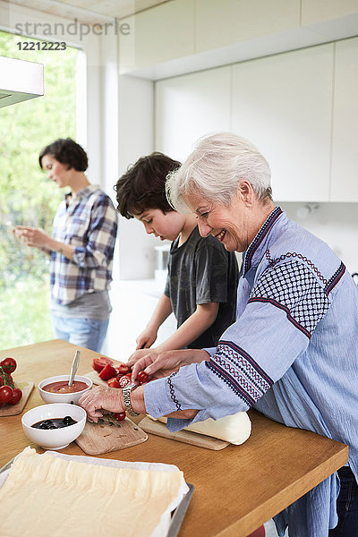 Großmutter und Enkel bereiten das Essen in der Küche zu  Mutter im Hintergrund