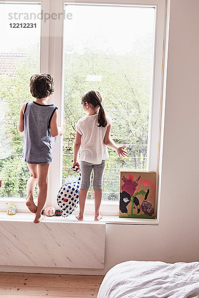 Bruder und Schwester schauen aus dem Fenster  Rückansicht