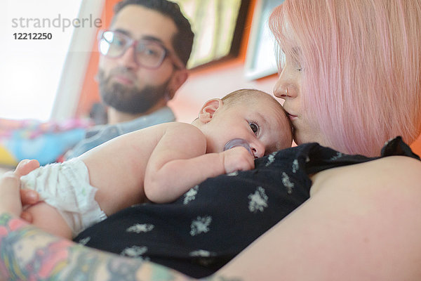 Frau mit Baby Junge auf der Brust  Ehemann im Hintergrund