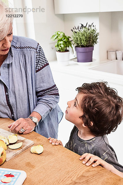 Großmutter und Enkel bereiten das Essen in der Küche zu  Enkel mit fragendem Gesichtsausdruck