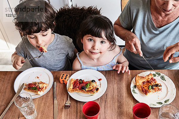 Großmutter sitzt mit Enkelkindern am Küchentisch  isst Pizza  erhöhte Ansicht