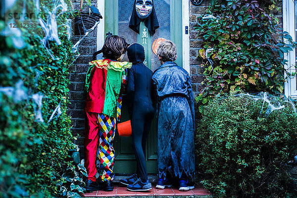 Drei Jungen in Halloween-Kostümen  an der Tür stehend  Süßes oder Saures  Rückansicht