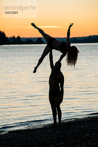 Ehepaar praktiziert Yoga am Strand bei Sonnenuntergang