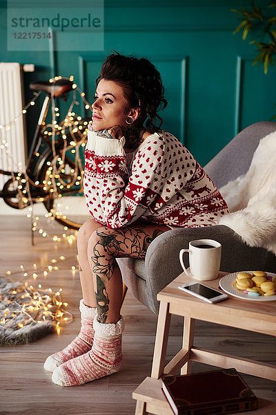 Junge Frau sitzt zu Hause  trägt Weihnachtspullover  nachdenklicher Gesichtsausdruck