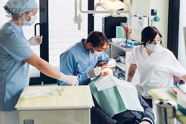 Zahnarzt schaut in den Mund des männlichen Patienten  Zahnarzthelferinnen bereiten Ausrüstung vor