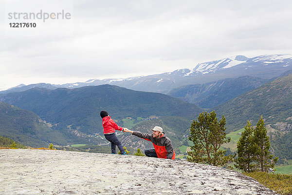 Junge hilft Wandervater über Fels in Berglandschaft  Jotunheimen-Nationalpark  Lom  Oppland  Norwegen
